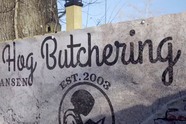 Film still of a sign that reads Hog Butchering, Est. 2003.