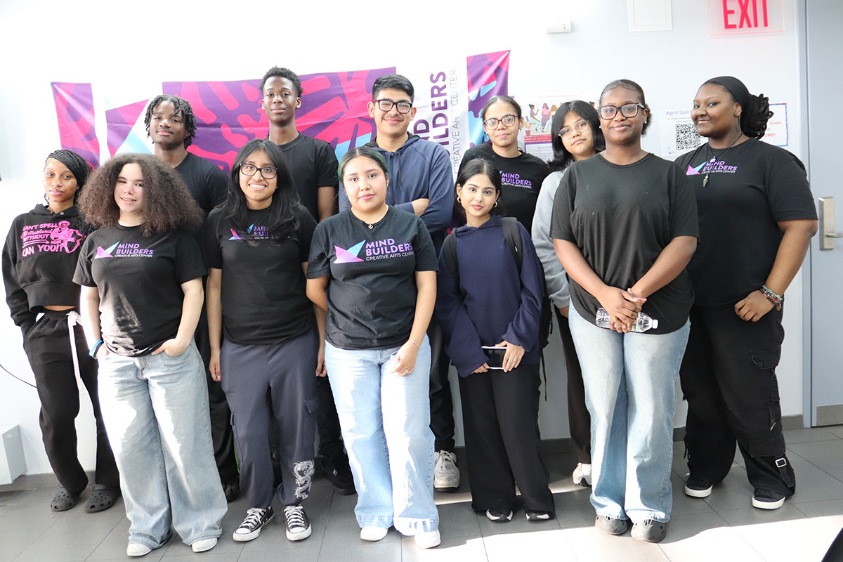 Twelve teens and young adults pose standing and smiling. Many wear black shirts with the pink, purple, and blue Mind Builders logo.