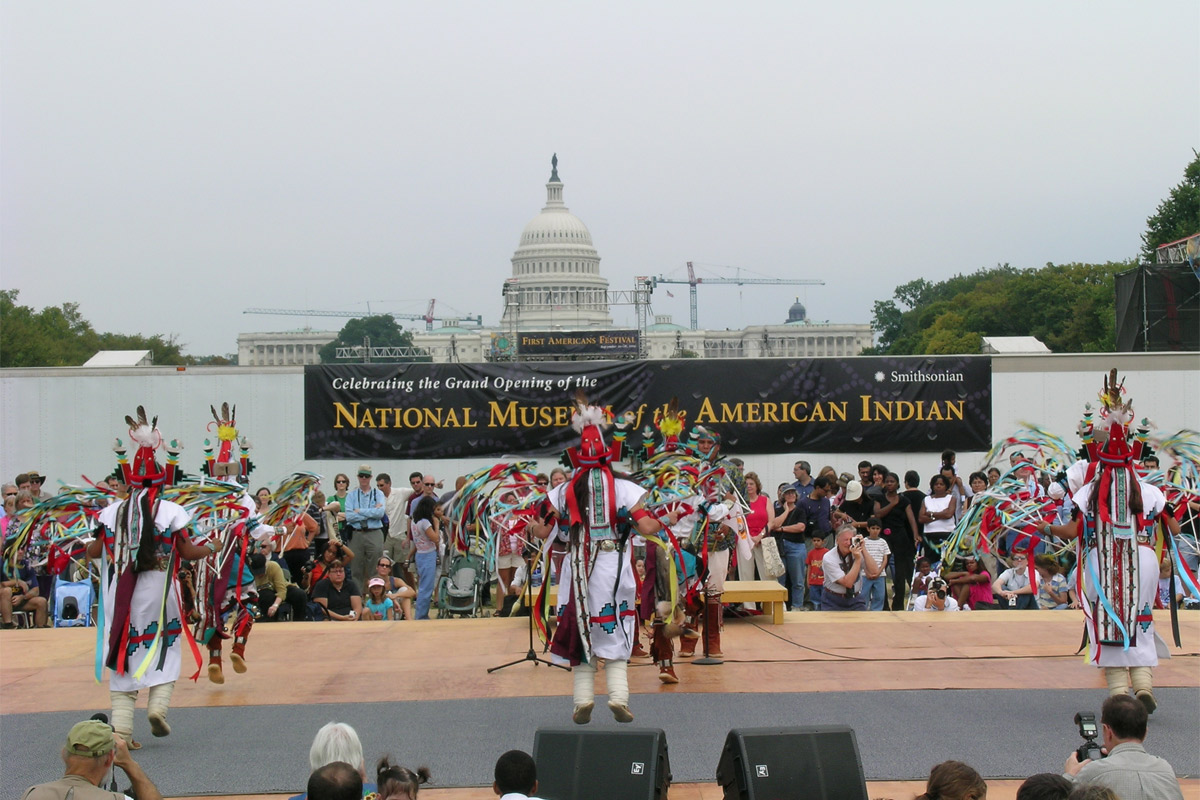 Native dancers perform on an outdoor stage with the U.S. Capitol Building in the background.