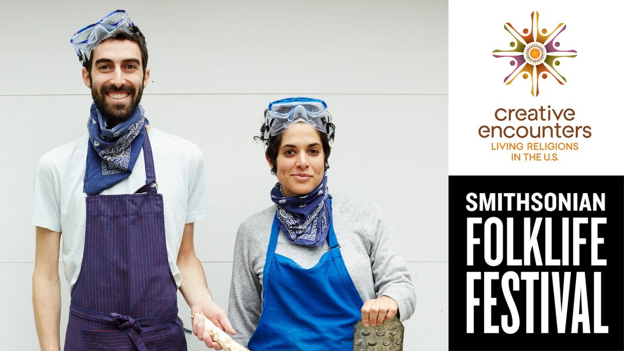Two people in aprons with lab goggles above their heads smile into the camera.