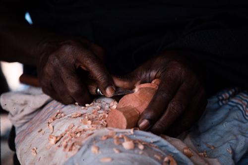 Close-up on a pair of hands carving a piece of wood with a metal tool.