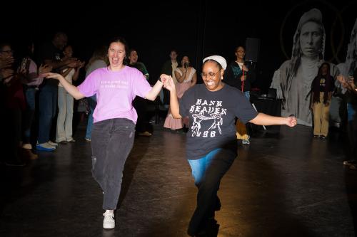 Two people dance among a crowd, holding hands and smiling broadly.