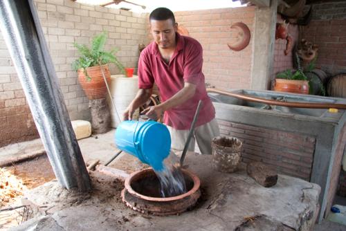 Water and fermented maguey are poured into a brick still or alambique for mezcal distillation.