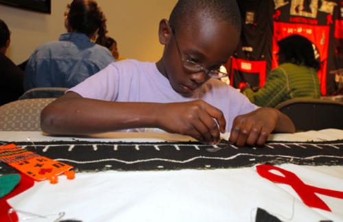 A boy takes part in a Call My Name workshop in Houston, Texas, by sewing fabric cut-outs onto a panel.