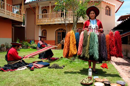 A woman holds up a rack of yarn dyed with rich natural colors: golds, greens, and reds.