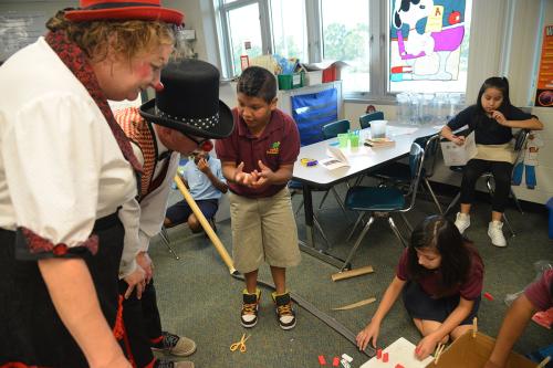 A fifth-grade student explains the engineering process with clowns Karen Bell and Robin Eurich.