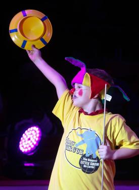 A first grader triumphantly holds up his plate after successfully spinning it in the Circus Sarasota Big Top with Build-a-Circus.