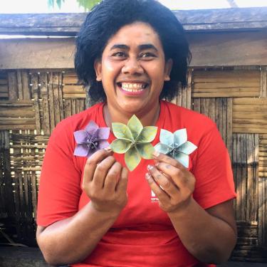 A woman smiles, holding up three cloth flowers.