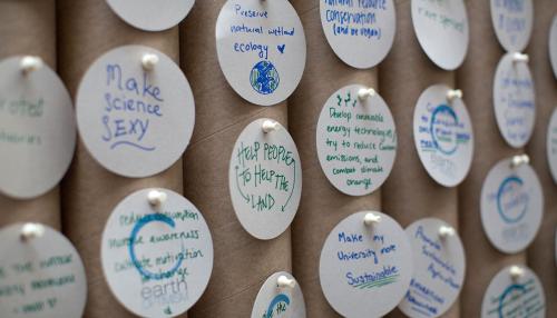 Several circular notes thumb-tacked to a surface that appears to be made of cardboard paper towel tubes. Notes read: “Make science sexy,” “Help people to help the land,” “Preserve natural wetland ecology” with a picture of the Earth and a heart, “Make my 