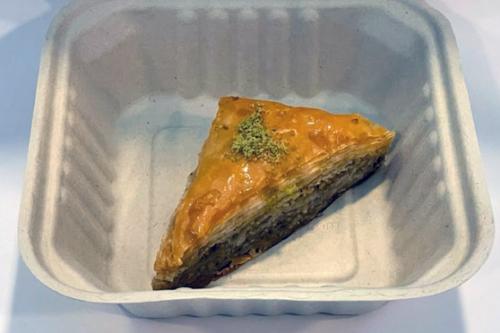 Triangular piece of layer pastry with greenish filling and green pistachio dust on top.