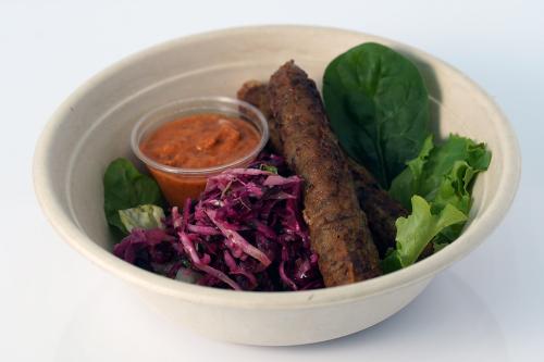 Bowl of brown sausage, purple cabbage, lettuce greens, and cup of red sauce.