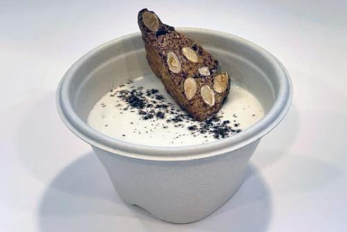 Cup of white pudding-like dessert with a tan biscotti, showing sliced almond baked in, on top.