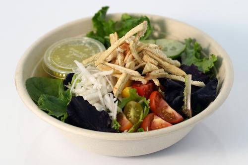 Bowl of salad with lettuce greens, red cherry tomatoes, strips of pita bread, and a small cup of dressing.