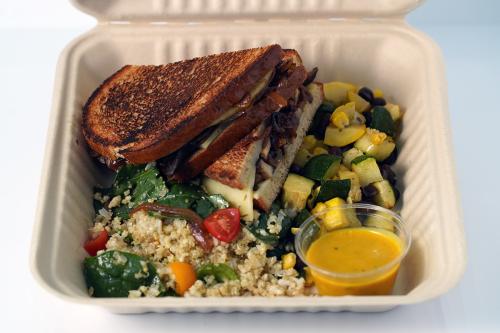 Toasted sandwich filled with cheese and mushrooms, alongside grain and vegetable salads, with a cup of yellow dressing.