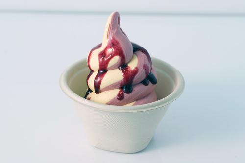 Cup of pink and white swirled soft serve with a red syrup drizzled on top.