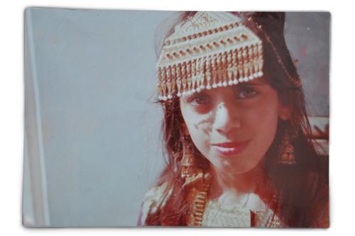 A young woman smiles, a triangular beaded ornament hanging over her forehead, and matching earrings and necklace. Old color photograph.