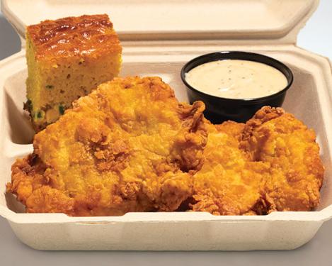 Pieces of fried chicken and yellow cornbread with white sauce in a cardboard container.