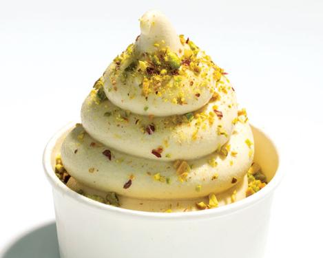 Swirl of white ice cream with dusting of greenish brown ground nuts in a paper cup.