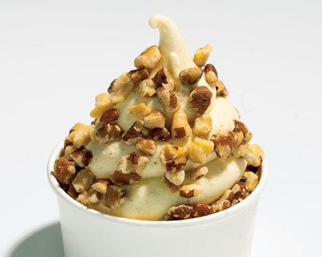 Swirl of white ice cream topped with chunks of brown walnuts in a paper cup.