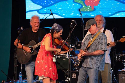 Four people play guitars and fiddle on stage.