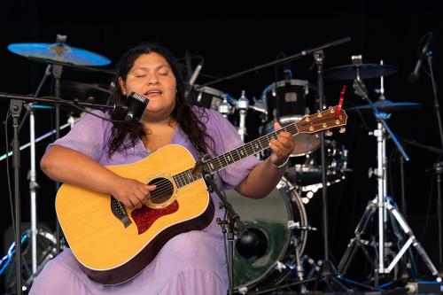 A woman strums a guitar and sings on stage.