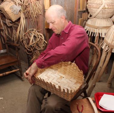 Aaron Holsapple, seated, works on weaving a basket.