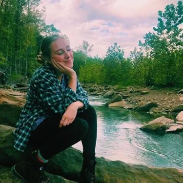 A woman seated and smiling by a river.