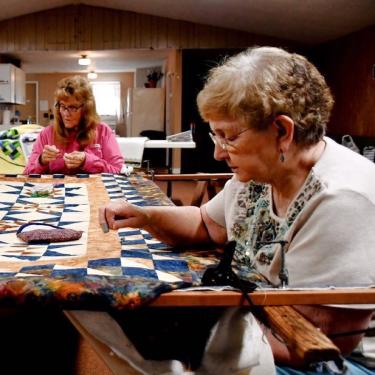 Two women work on a quilt over a table.