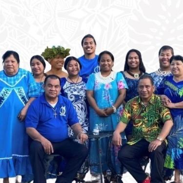 A group of people in blue Marshallese dress stand shoulder to shoulder.