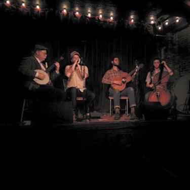 Four-piece string band playing on dark stage.