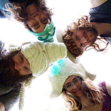 Four people looking downward at the camera, bright white sky behind them.