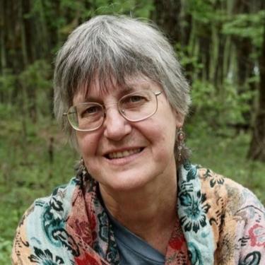 A woman in glasses smiles in the woods.