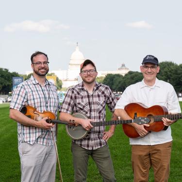 Three men holding a fiddle, banjo, and acoustic guitar.