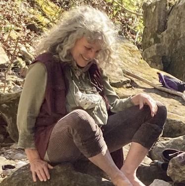 A woman sits barefoot amidst rocks.