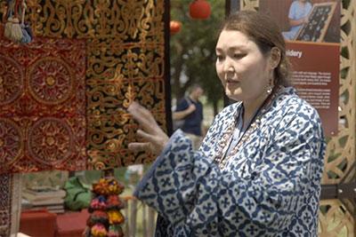A woman in a blue and white patterned dress gestures with one hand. 