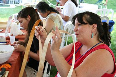 Women sit at a table weaving strips of plant fiber.