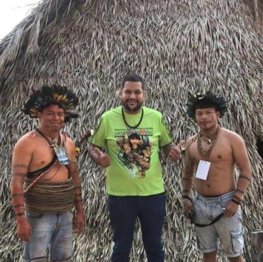 Three men posed in front of a thatched structure.
