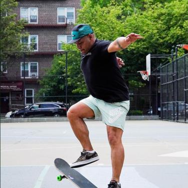 A man wearing a black t-shirt and blue shorts skateboarding.