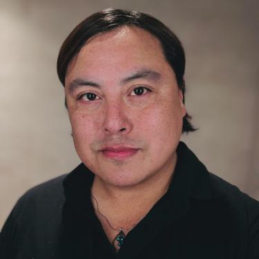 A man wearing a black shirt on a plain background.