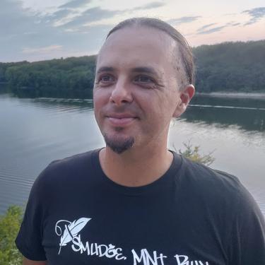A man wearing a black t-shirt standing in front of a body of water.