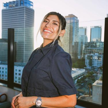 A smiling woman standing in front of a city skyline.