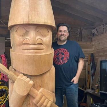 A man stands next to a hand-carved totem.