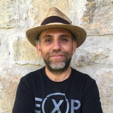 A man wearing a black shirt and a woven hat.