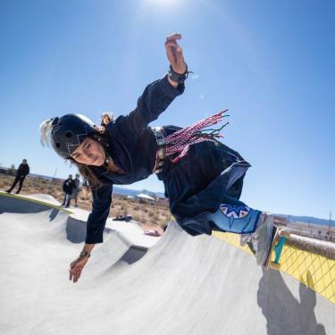 A woman with a fringed belt skateboarding on a halfpipe.
