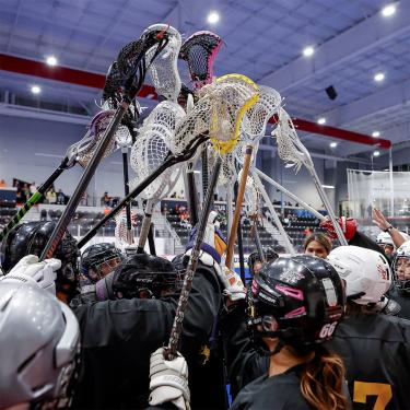 A team of men's lacrosse players lifting their sticks in the air.