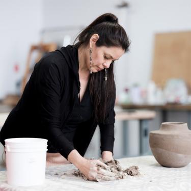A woman standing at a table, working with clay.