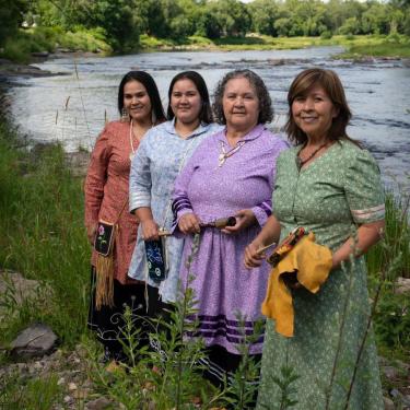 Four women in floral dresses posed by a river.