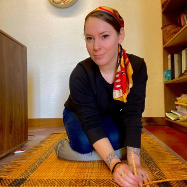 A woman kneeling over a weaving project.