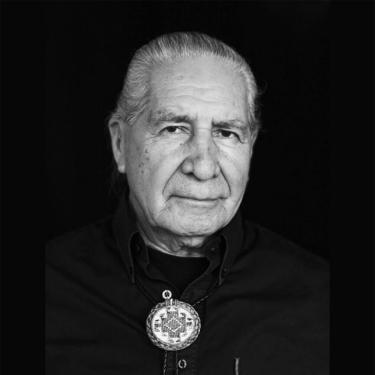 A man wearing a black button up shirt and a beaded bolo tie.