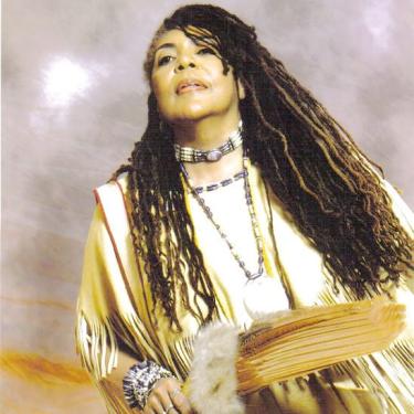A woman with dreadlocks wearing beads and holding a fan.